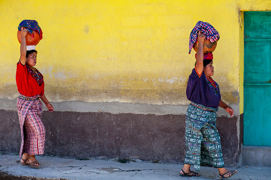 Maya women in traditional dress in front of a yellow house wall